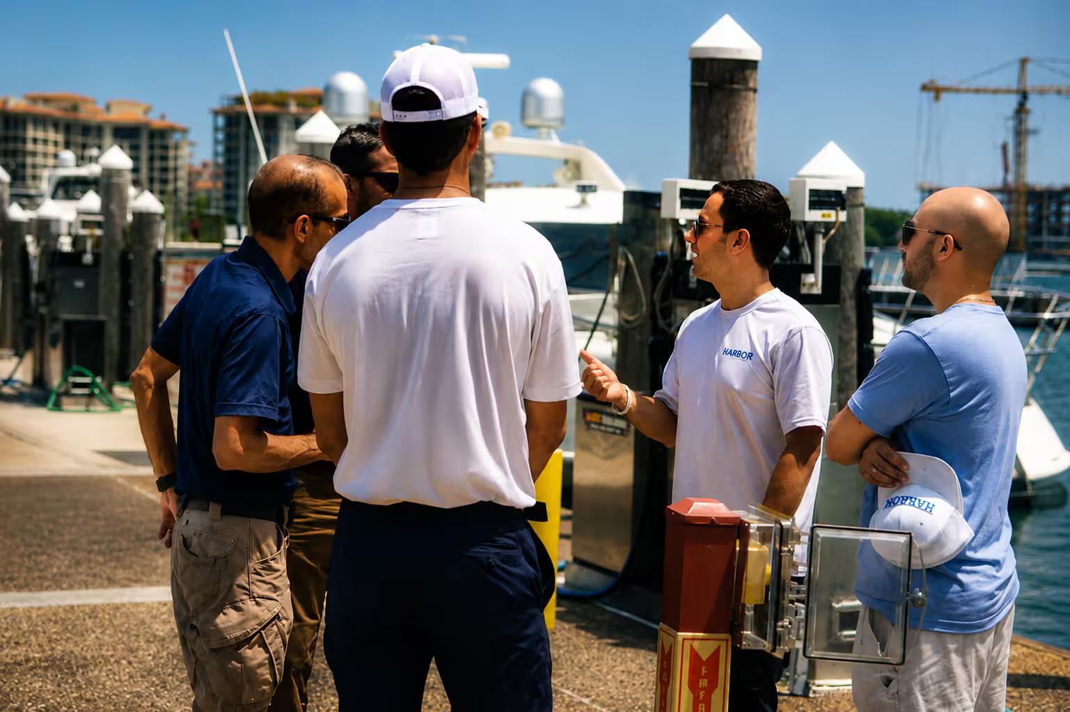 Harbor's branded booth at a marina dock event, the team talking with visitors, yachts and the waterfront skyline behind.