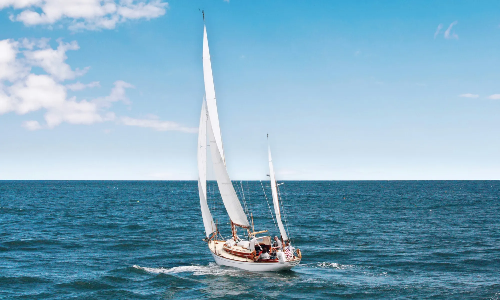 A sailing yacht under full sail on open water on a clear day.